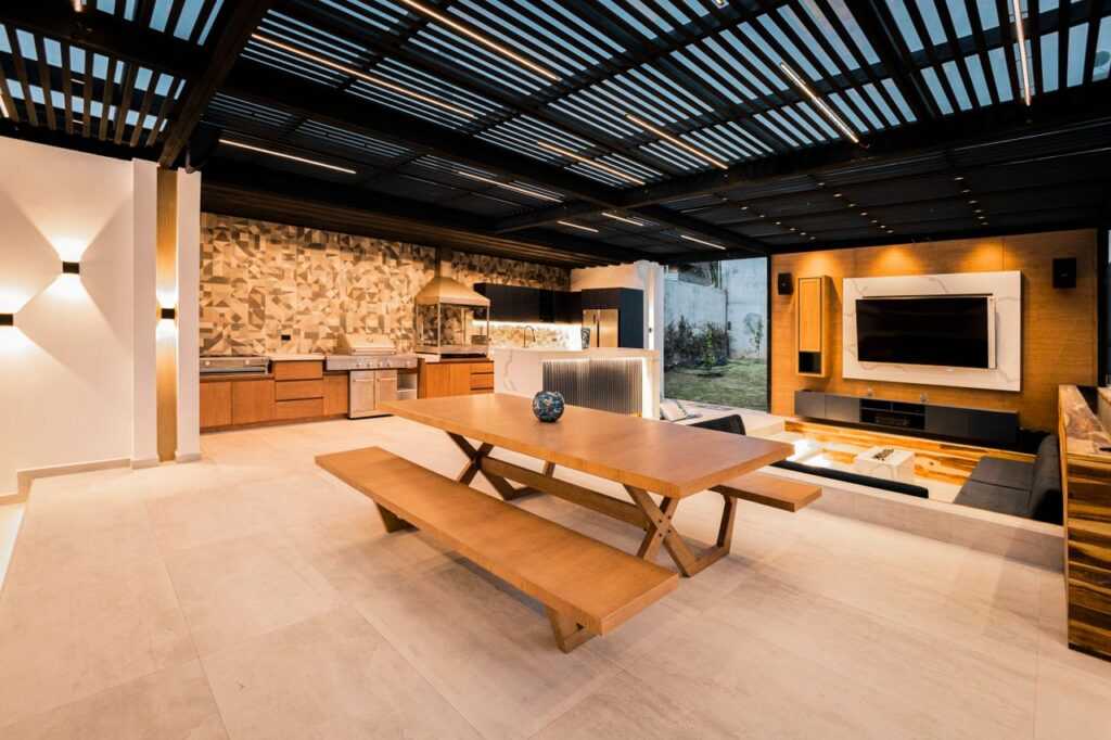 Spacious outdoor kitchen and living space featuring sleek design, wood accents, and a mounted TV.