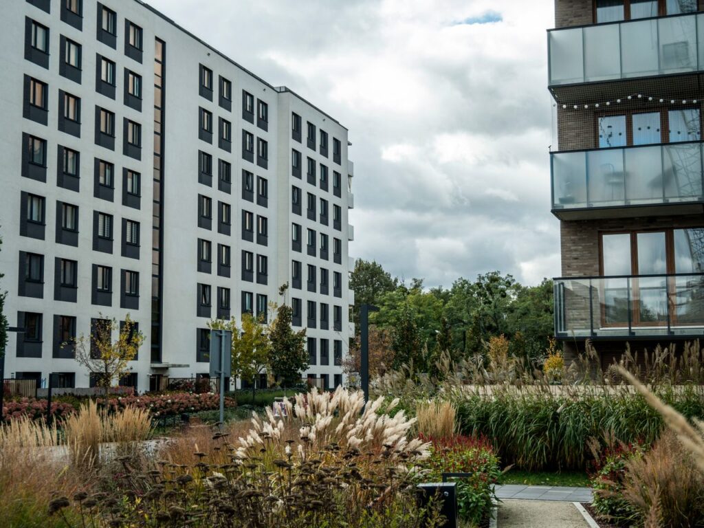 Apartment buildings with garden and tall grasses under cloudy skies.